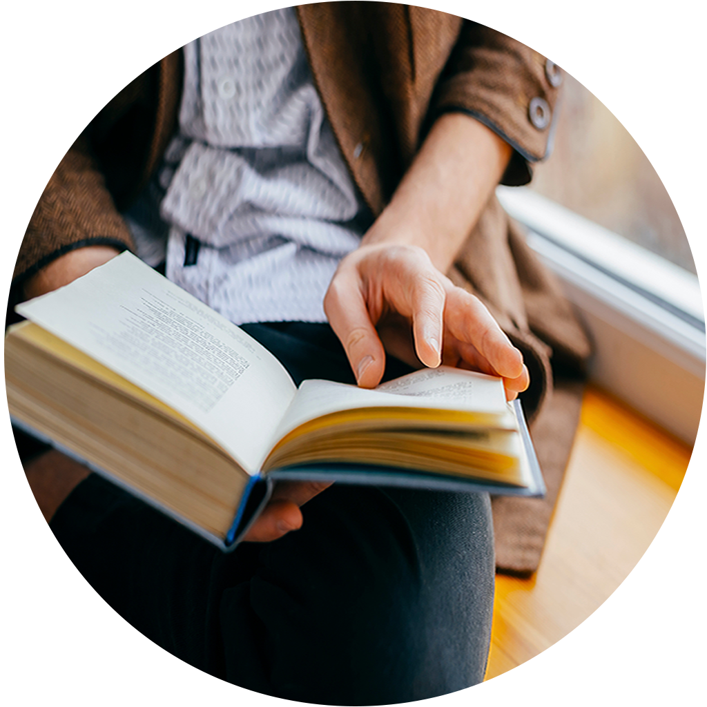 A person sitting by a window, holding an open book.